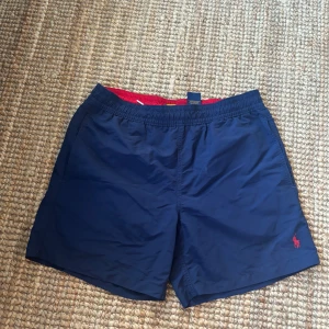 mörkblåa badshorts från Polo Ralph Lauren - Säljer ett par polo ralph lauren badshorts i fint skick dock har de en liten skada på baksidan ( se bild 5 ) kolla gärna in min sida och se vad ja mer har, skriv gärna om du har fler frågor ❣️❣️