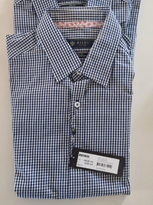 Blårutig slim fit skjorta Riley - Snygg blårutig skjorta från Riley i slim fit-modell. Skjortan har klassisk krage, knappar framtill och är tillverkad i mjuk bomull. Perfekt för dig som gillar stilrena och tidlösa plagg med modern passform. Pris för båda 