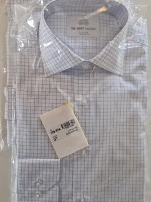 Blårutig skjorta från The Shirt Factory - Säljer en stilren blårutig skjorta från The Shirt Factory i slim fit-modell. Skjortan har klassisk krage, långa ärmar och knappar framtill. Materialet är mjuk bomull och mönstret består av tunna blå rutor på vit bakgrund. Perfekt för dig som gillar en clean och fräsch look. Pris för båda