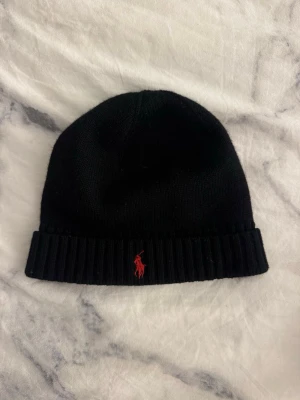 Svart mössa från Polo Ralph Lauren - Svart mössa från Polo Ralph Lauren. Köpt från kidsbrandtore och använd typ 1-2 vintrar. Storlek one Size 