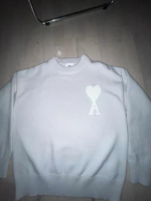 Beige stickad tröja från Ami - Säljer en vit stickad tröja från Ami Alexandre Mattiussi med rund hals och ribbade muddar. Tröjan har ett stort hjärta med bokstaven A broderat på bröstet. Perfekt för vintern för dig som inte gillar kyla.