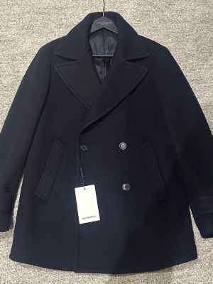 Mörkblå skepparkavaj från Suitsupply - Säljer en stilren mörkblå skepparkavaj från Suitsupply med breda slag, dubbelknäppning och två snedställda fickor. Jackan är tillverkad i ull och har en klassisk passform med långärmade ärmar. Jackan är HELT NY med prislapp kvar och har aldrig använts. Jackan är i storlek 44/xs men är stor i storlek så passar mer åt 46/s. 170-180 cm ca. Nypris 4699