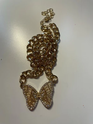 Guldfärgat halsband med fjärilshänge - Säljer ett chunky guldfärgat halsband med ett  fjärilshänge dekorerat med små glittriga stenar💞 