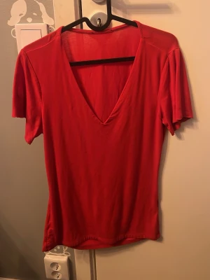 Röd v-ringad topp med kort ärm - Passar s/m/k Säljer en röd topp med djup v-ringning och korta ärmar. Tunn och mjuk i materialet, perfekt för varmare dagar. Passformen är normal och toppen har en enkel, stilren design utan mönster eller extra detaljer.