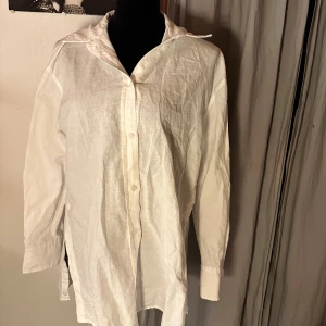 Vit långärmad skjorta från Zara - Vit skjorta från Zara i storlek S, tillverkad i ett lätt och luftigt linnematerial. Skjortan har klassisk krage, knappar framtill och långa ärmar med manschett. Perfekt för dig som gillar en clean och enkel stil.