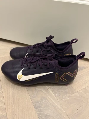 Nike Air Zoom Mercurial MBAPPE fotbollsskor  - Säljer ett par Nike Air Zoom Mercurial Vapor 16 academy MG MBappe personal edition fotbollsskor i mörklila med vita och guldiga detaljer. Skorna har snörning, platt sula med dobbar och coola KM- och Mercurial-tryck på sidan och hälen. Perfekt för dig som vill sticka ut på planen! Superbra skick, som nya! Storlek 37,5