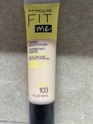 Maybelline Fit Me Tinted Moisturizer 103 - Maybelline Fit Me Tinted Moisturizer i nyansen 103, 30 ml. Ger lätt täckning och återfuktar huden med aloe. Passar alla hudtyper och innehåller 76% ingredienser av naturligt ursprung. Tuben är beige med svart och gul text.