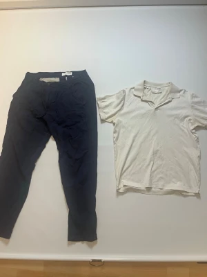 Mörkblå byxor & en vit Piké från Selected Homme storlek L - Snygga mörkblå chinos från Selected Homme i storlek L. Byxorna har klassisk passform med raka ben och sidfickor samt bakfickor med knapp. Materialet är mjukt och känns som bomull, perfekt för en chill och stilren look. Det är också en vit piké från selected Homme båda är med på köpet för endast 99kr båda är också 99kr