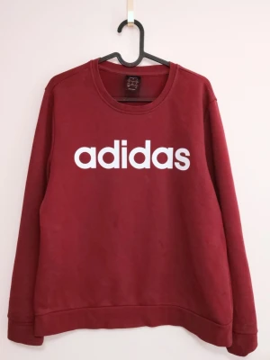 Röd Adidas sweatshirt med tryck - Säljer en röd sweatshirt från Adidas i storlek L. Tröjan har ett stort vitt Adidas-tryck på bröstet och är långärmad med rund hals. .Det finns en liten fläck på höger ärm som kan tas bort med borttagsmedel. Därav priset 