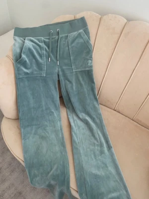Gröna mjukisbyxor från Juicy Couture XS - Snygga gröna mjukisbyxor från Juicy Couture i storlek XS. Byxorna har bred resår i midjan med snörning, stora fickor fram och bak med knappdetaljer. Materialet är mjuk sammet som ger en lyxig känsla och relaxed vibe. Dom är i ett jättebra skick , har inte använt på några år. Pris kan sänkas vid snabb affär