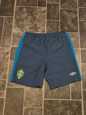 Umbro Fotbollsshorts SvFF - Umbro fotbollsshorts i storlek M med Svenska Fotbollförbundets märke. Mörkblå träningsshorts med resår i midjan och fickor med dragkedja. Bekväma och lätta, passar bra för träning och sport. Aldrig använda💕