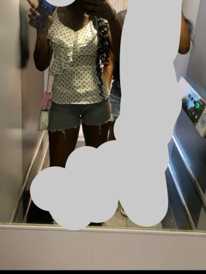 Vit prickig blus med volang - Säljer en vit blus med svarta prickar och volangdetaljer framtill. Blusen har v-ringad hals och är ärmlös. Materialet känns lätt och luftigt, och passformen är normal. Pris kan diskuteras💞