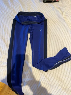 Nike Dri-Fit blå träningsbyxor S - Snygga blå Nike Dri-Fit träningsbyxor med svarta paneler längs sidorna. Byxorna har snörning i midjan, dragkedjor vid bensluten och är gjorda i ett syntetmaterial som andas. Perfekta för dig som gillar att träna och vill ha bekväma tights med bra passform. Jag har aldrig använt dem, men fick i present och klippte av taggen när jag provade dessa.