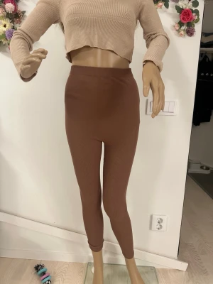 för gravida kvinnor - Säljer ett par bruna ribbade leggings med hög midja. De är stretchiga och sitter tight, perfekta för en chill och bekväm look. Materialet är mjukt och följsamt, och färgen är en varm brun ton som passar till det mesta.
