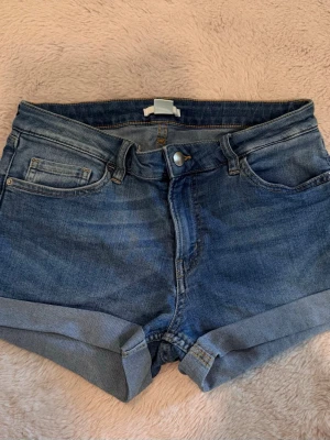 Blå jeansshorts med uppvik - Snygga blå jeansshorts med klassisk femficksdesign och uppvikta benslut. Modellen har normal passform och stängs med knapp och dragkedja framtill. Perfekta för varma dagar och har en cool, avslappnad vibe.