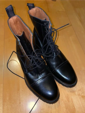 Svarta kängor från Roberto Ley - Säljer ett par svarta kängor från Roberto Ley i äkta skinn. Aldrig använda. De har robust sula med grovt mönster, snörning framtill och dragflikar bak. Insidan är i ljust läder och de har rund tå. Perfekta för dig som vill ha klassiska boots med snygg edge. De är tillverkade för hand i Spanien och det är ett märke med hög kvalité skor.  Priset är inte hugget i sten. Skriv vid minsta fråga!