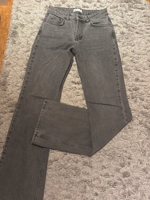 Grå jeans från Gina Tricot - Snygga grå jeans från Gina Tricot i utsvängd modell. Jeansen har en neutral grå färg. Har små defekter nertill och en liten defekt på bakre lår vilket man kan se i bilderna. Dessa defekter syns knappt. Mid waist. Säljer för att det är för små. 