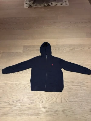 Polo Ralph Lauren Hoodie  - Klassisk mörkblå  hoodie från Polo Ralph Lauren i storlek 160. Tröjan har dragkedja, huva och två fickor framtill. Tillverkad i mjuk och skön bomullsblandning med den ikoniska broderade loggan på bröstet. I bra skick. Frakt ingår ej. Hör av dig om du vill ha fler bilder.