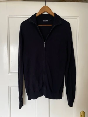 Svart kofta med dragkedja Brave Soul - Svart kofta från Brave Soul i storlek M. Tröjan har hel dragkedja framtill, ribbade muddar och hög krage. Materialet är mjukt och stickat, perfekt för kyliga dagar. Enkel och stilren design som funkar till många olika outfits.