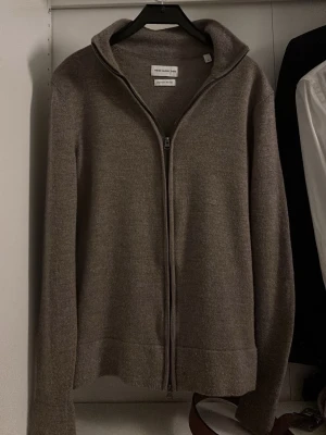 Brun merinoull cardigan från These Glory Days - Säljer en brun cardigan i merinoull från These Glory Days, storlek S. Koftan har hel dragkedja framtill och en hög krage. Materialet är mjukt och värmande merinoull, perfekt för kyliga dagar. Enkel och stilren design som funkar till många olika outfits.