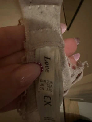 Rosa/lila spets-bh från Love, 70A - Säljer en beige bh från Love i storlek 70A. Bh:n har vackert blommigt spetsmönster över hela kuporna och tunna, justerbara axelband. Materialet är mjukt och har en elegant känsla med fina spetsdetaljer längs kanterna.