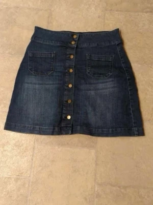 Mörkblå jeanskjol med knappar - Säljer en mörkblå jeanskjol med framfickor och snygga guldfärgade knappar hela vägen framtill. Kjolen har en klassisk A-linjeform och är perfekt för dig som gillar en enkel men trendig look.