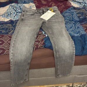 Grå jeans från Nudie Jeans - Snygga grå jeans från Nudie Jeans med klassisk femficksdesign och ljus tvätt. Byxorna har raka ben och coola broderade detaljer på bakfickorna. Tillverkade i bomull för en skön känsla och stilren look. Dom är äkta och kvittobevis finns om ni frågar om det. Aldrig använda och säljer dom pga att dom ej passade. 
