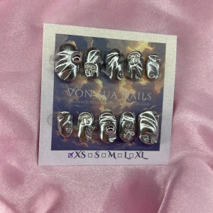 Silver (XS);ExtraShortOval  - Handgjorda press-on naglar i metallic silver med unik 3D-effekt och små stenar. Naglarna har en vågig, abstrakt form och kommer i XS: 14 mm, 11 mm, 11,5 mm, 10 mm, 8 mm . Perfekt för dig som vill sticka ut med en edgy och modern look.