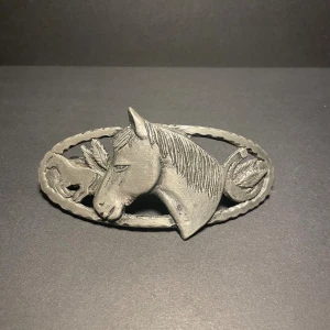 Silvrig hårklämma med hästmotiv - Unik hårklämma i silverfärgad metall med detaljerat motiv av en häst. Oval form och robust spänne på baksidan. Perfekt för dig som älskar hästar och vill ha en cool accessoar som sticker ut.