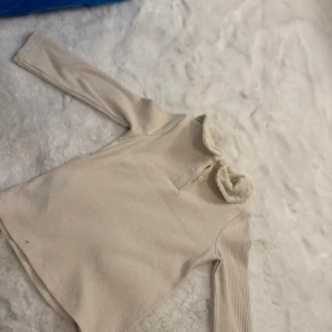 Beige ribbad pikétröja med spetskrage - Supersöt beige pikétröja från LC Waikiki med ribbad struktur och långärmad passform. Tröjan har en spetsig krage med broderade detaljer och knappar framtill. Perfekt för dig som gillar en gullig och stilren look.