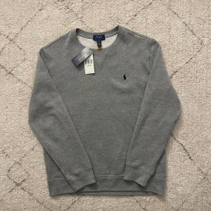 Grå sweatshirt från Polo Ralph Lauren - Snygg grå sweatshirt från Polo Ralph Lauren i storlek xl fast i barn model/ passar storlek s, tröjan är ny och helt oanvänd - priset kan diskuteras 