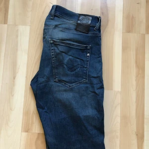 Replay jeans blå med slitningar - Säljer ett par snygga Replay jeans i mörkblå tvätt med slitningar och hål på knäna. Klassisk femficksmodell med raka ben och läderpatch bak i midjan. Jeansen har coola detaljer och är tillverkade i jeansmaterial med skön passform.