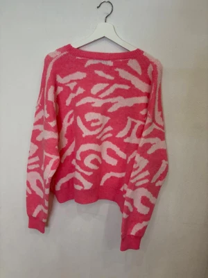 Rosa och vit stickad tröja med mönster - Säljer en mysig stickad tröja från SHEIN  i rosa och vitt med ett coolt abstrakt mönster. Tröjan har rund hals, långärmade ärmar och en loose passform som ger en chill vibe. Perfekt för att addera färg till din garderob.