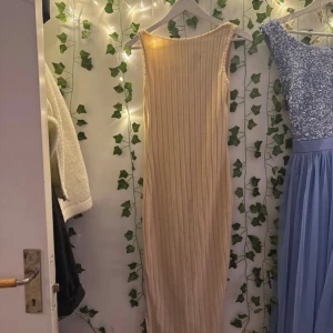 Beige ribbad långklänning - Säljer en beige långklänning med ribbad struktur och ärmlös design. Klänningen har en rundad halsringning och är figurnära med en stilren look. Perfekt för dig som gillar minimalistisk stil och mjuka färger.
