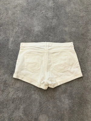 Vita shorts med fickor från H&M - Snygga vita shorts från H&M med klassisk femficksdesign och uppvikta benslut. De har gylf med dragkedja och knapp i guldton. Perfekta för varma dagar och enkla att matcha med allt. Materialet är mjuk bomull som känns skönt mot huden.