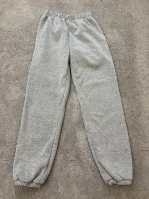 Grå mjukisbyxor med resår - Gråa mjukisbyxor med elastisk midja och muddar vid bensluten. Perfekta för chill dagar eller när du vill vara extra bekväm. Tillverkade i mjukt bomullsmaterial som känns skönt mot huden.