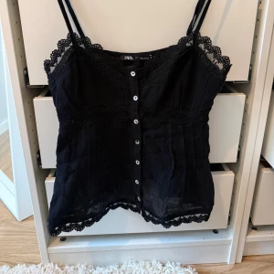 Svart topp från Zara - Supersöt svart linnetopp från Zara med tunna axelband och dekorativ spets längs kanterna. Storlek S och aldrig använd