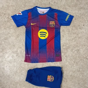 FC Barcelona Lamine Yamal matchtröja - Säljer en FC Barcelona matchtröja med Lamine Yamal och nummer 10 på ryggen. Tröjan är kortärmad med klassiska blå och röda vertikala ränder, gula detaljer och klubbmärke på bröstet. Materialet är lätt och andas, perfekt för fotboll. Shorts med klubbmärke ingår.