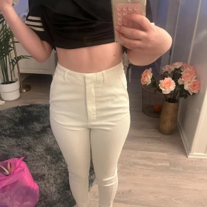 Vita kostymbyxor  - Snygga vita kostymbyxor från Bik Bok i ankellängd, storlek 36. De är högmidjade med smal passform och har diskreta fickor bak. Materialet är mjukt och känns som bomull med lite stretch. Perfekta till sneakers eller boots för en clean look.