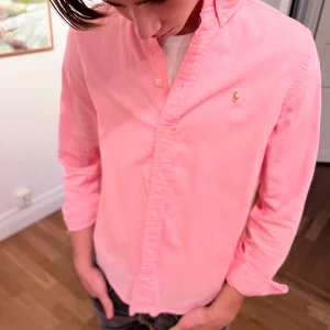 Rosa skjorta från Ralph Lauren - Snygg rosa skjorta från Ralph Lauren med klassisk krage och broderad logga på bröstet. Skjortan är gjord i mjuk bomull. Perfekt för dig som vill ha en fräsch och stilren look.