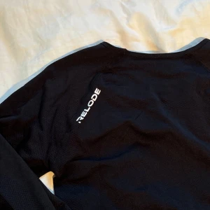 Svart långärmad träningströja från Relode - Svart långärmad lite cropped träningströja från Relode med vit logga på axeln!