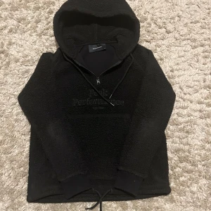 Svart Peak Performance fleece hoodie XS - Mysig svart hoodie från Peak Performance i fleece med broderad logga på bröstet. Tröjan har huva, snörning nedtill, half zip och långa ärmar. Perfekt för kalla dagar och chill stunder. Snygg och enkel att matcha med jeans eller mjukisbyxor.