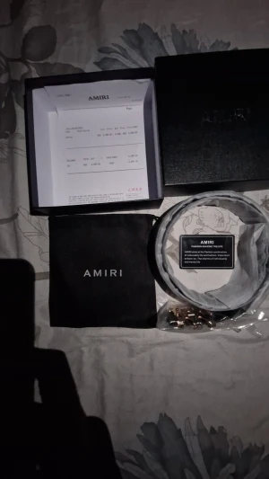 Svart skärp från Amiri med guldspänne - Snyggt svart bälte från Amiri i äkta skinn med ett unikt guld- och svartfärgat metallspänne i form av Amiris logga. Bältet är stilrent och passar perfekt till jeans eller kostymbyxor. Levereras med originalbox och dustbag.