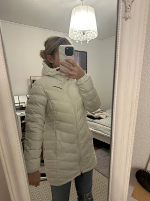 Vit dunjacka Peak Performance XS - Säljer en vit dunjacka från Peak Performance i storlek XS. Jackan har huva, lång ärm och snygg quiltad design med dragkedja framtill. Perfekt för kalla dagar och har en clean look med diskret logga på bröstet. Passar dig som gillar funktionell vinterjacka. Passar även att åka skidor med. Pris går att diskutera 