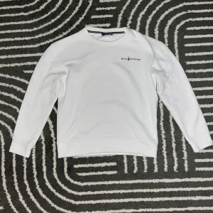 Vit Sail Racing sweatshirt - Vit sweatshirt från Sail Racing med diskret logga på bröstet och en liten logga i nacken. Tröjan har rund halsringning och långa ärmar. Tillverkad i mjuk bomullsmix som är skön att bära. Perfekt för en clean och stilren look.