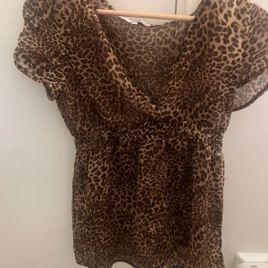 Leopardmönstrad blusTally Weijl - Säljer en söt blus från Tally Weijl i transparent, lätt material med leopardmönster. Modellen har v-ringning, korta ärmar och smockad midja som ger en snygg siluett. Perfekt för dig som vill sticka ut med ett djurmönstrat plagg.