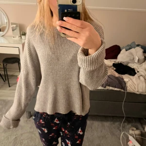 Grå ribbad stickad tröja - Mysig grå stickad tröja med ribbad struktur och långa ärmar. Tröjan har en loose passform och breda muddar vid ärmsluten som kan vikas upp för en chill look. Perfekt för att hålla sig varm under kyliga dagar.