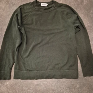 Mörkgrön tröja från East West - En stilren mörkgrön tröja från East West med rund hals och långa ärmar. Tröjan har en enkel design utan mönster eller detaljer.  Materialet känns mjukt och bekvämt mot huden.