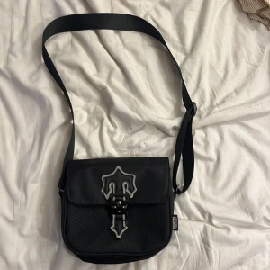 Svart axelväska från Trapstar - Snygg svart axelväska från Trapstar med justerbar rem och unik reflexdetalj. Väskan har coolt spänne framtill och meshmaterial på nedre delen. 