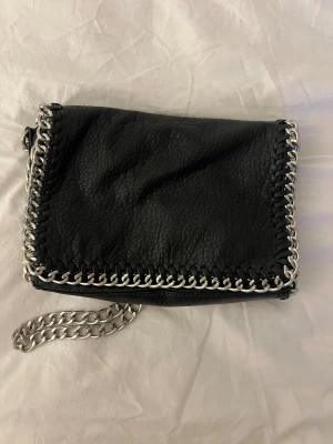 Svart axelväska med kedjedetaljer - Super snygg äkta TIAMO väska i skin! Säljer då den inte kommer till så mycket användning längre 💕💕